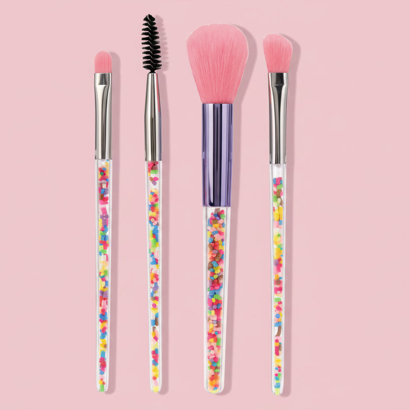 Set of four makeup brushes with colorful, sparkly handles on a pink background