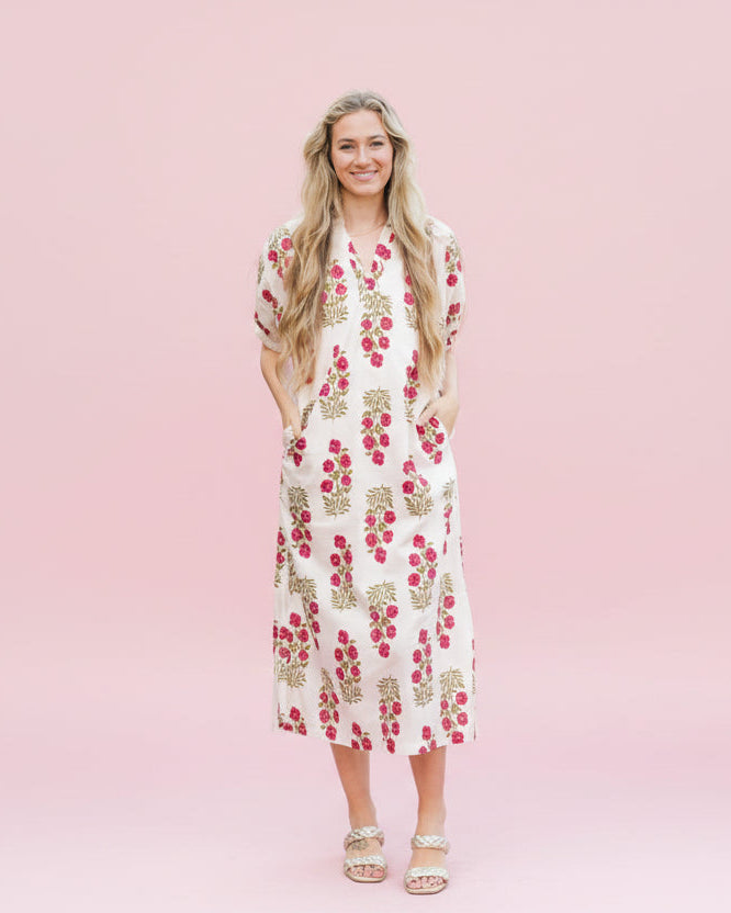 Woman in a floral dress standing on a cobblestone street with an American flag in the background.