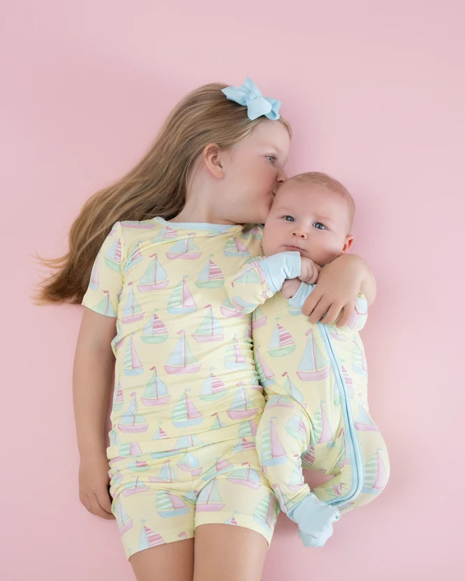 Two children in matching pastel outfits with sailboat pattern on a pink background