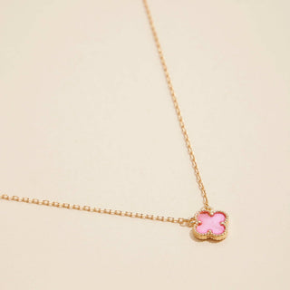 Gold necklace with a clover pendant on a light pink background
