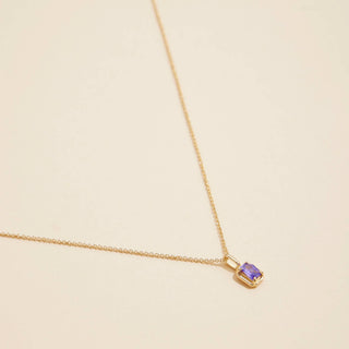 Gold birthstone pendant necklace on a beige background. 