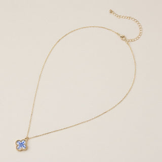 Gold necklace with a blue pendant on a beige background