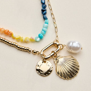 Jewelry set with gold chain, shell charm, and pearl on a light background