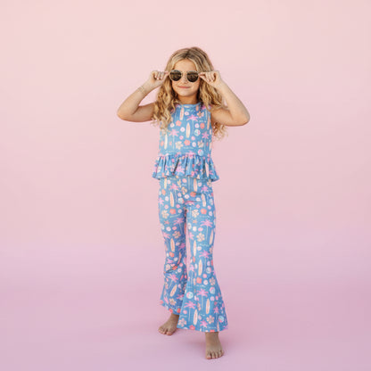 Young girl in a colorful jumpsuit standing on a pink background.