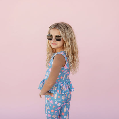 Child wearing a blue floral jumpsuit on a pink background 