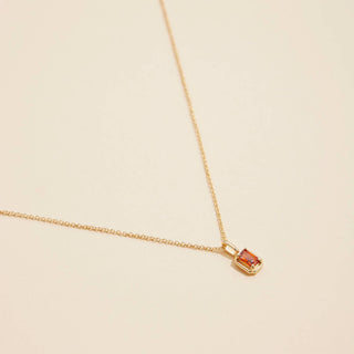 Gold birthstone pendant necklace on a beige background. 