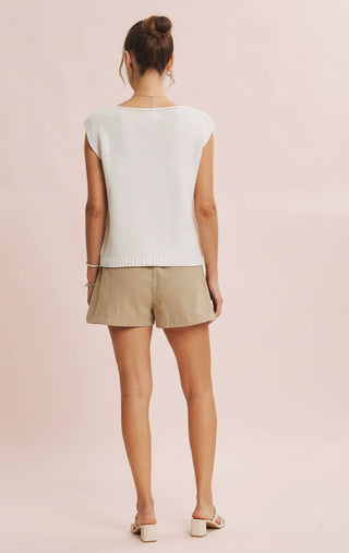 Woman wearing a white sleeveless top and beige shorts on a pink background