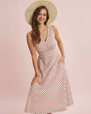 Woman wearing a striped dress and straw hat on a pink background