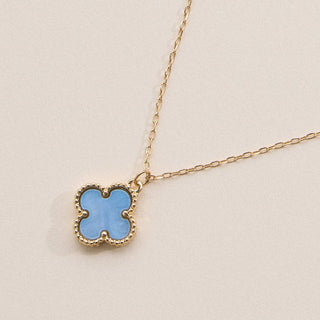 Gold necklace with a clover pendant on a light pink background