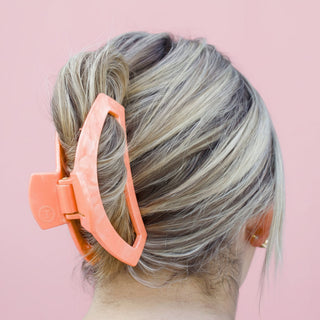 Person with a bun wearing an orange hair clip against a pink background