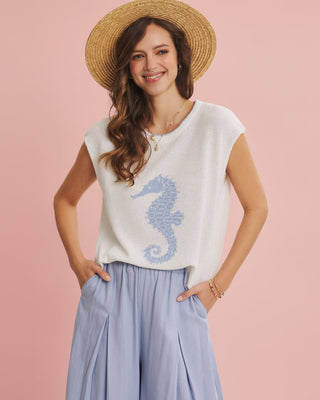 Woman wearing a sleeveless top with a seahorse design and light blue pants on a pink background