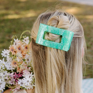 Person with a green hair clip holding flowers outdoors