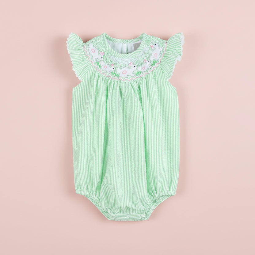 Green baby romper with floral embroidery on a pink background