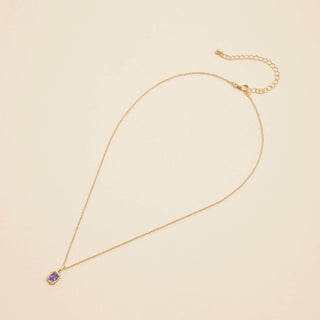 Gold birthstone pendant necklace on a beige background. 
