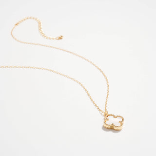 Gold necklace with a clover pendant on a light pink background