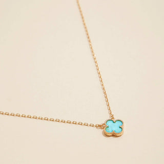 Gold necklace with a clover pendant on a light pink background