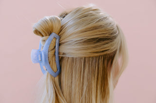 Close-up of a blue hair clip in blonde hair with a pink background