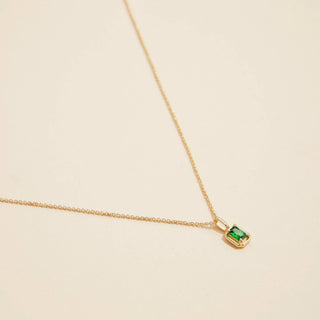 Gold birthstone pendant necklace on a beige background. 
