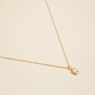 Gold birthstone pendant necklace on a beige background. 