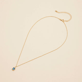 Gold birthstone pendant necklace on a beige background. 