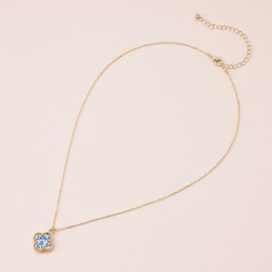 Gold necklace with a clover pendant on a light pink background