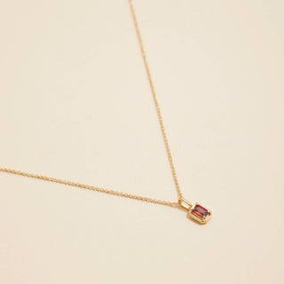 Gold birthstone pendant necklace on a beige background. 