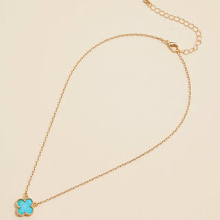 Gold necklace with a clover pendant on a light pink background