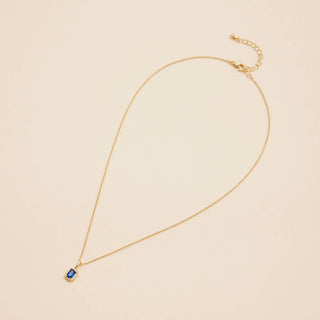 Gold birthstone pendant necklace on a beige background. 