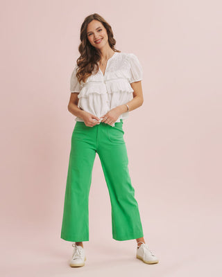 Woman wearing a white blouse and green pants on a pink background
