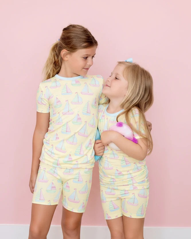 Two children wearing matching pajama sets with sailboat pattern on a pink background