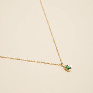 Gold birthstone pendant necklace on a beige background. 