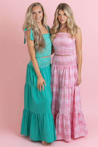 Two women wearing colorful tiered dresses on a pink background