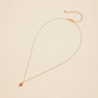 Gold birthstone pendant necklace on a beige background. 