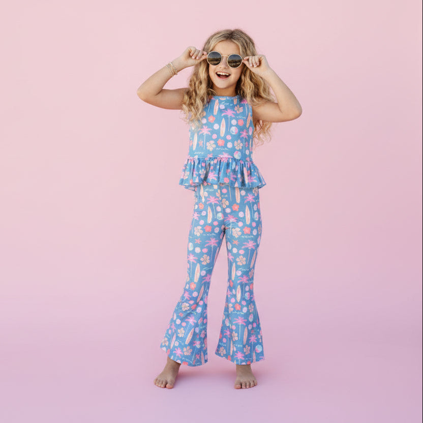 Young girl in a blue floral dress standing in front of a pink background. 