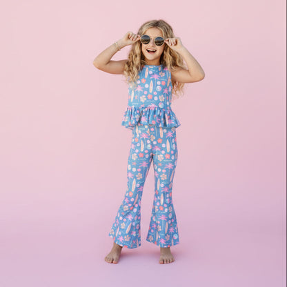 Young girl in a blue floral dress standing in front of a pink background. 