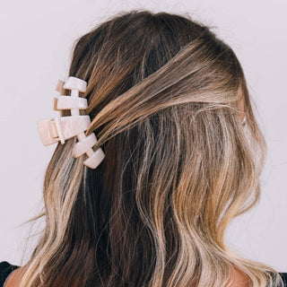 Person with wavy hair wearing a pink hair clip against a pink background