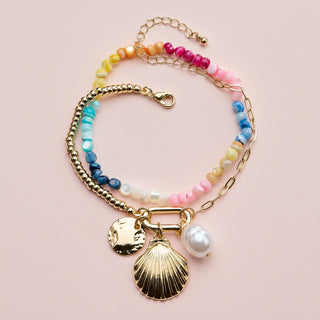 Multicolored beaded bracelet with gold chain and shell charm on a beige background