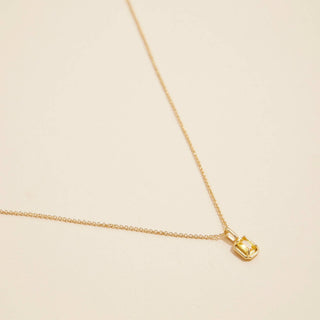 Gold Birthstone Pendant Necklace on a beige background. 