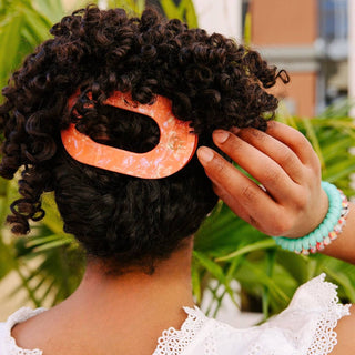 Person styling their hair with an pink hair clip outdoors
