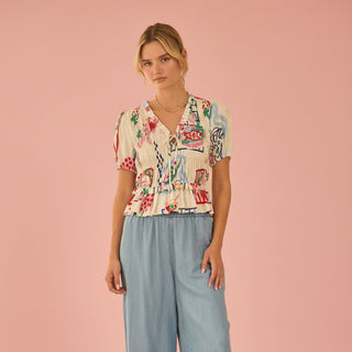 Woman wearing a patterned top and light blue wide-leg pants on a pink background