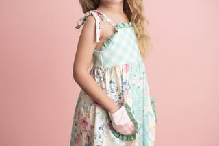 Child wearing a floral dress with green accents on a plain background