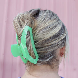 Green hair clip in a person's hair against a pink background