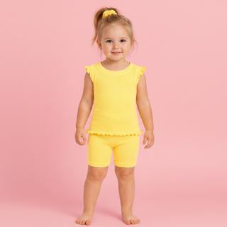 Child wearing a yellow outfit with ruffled sleeves and shorts on a pink background