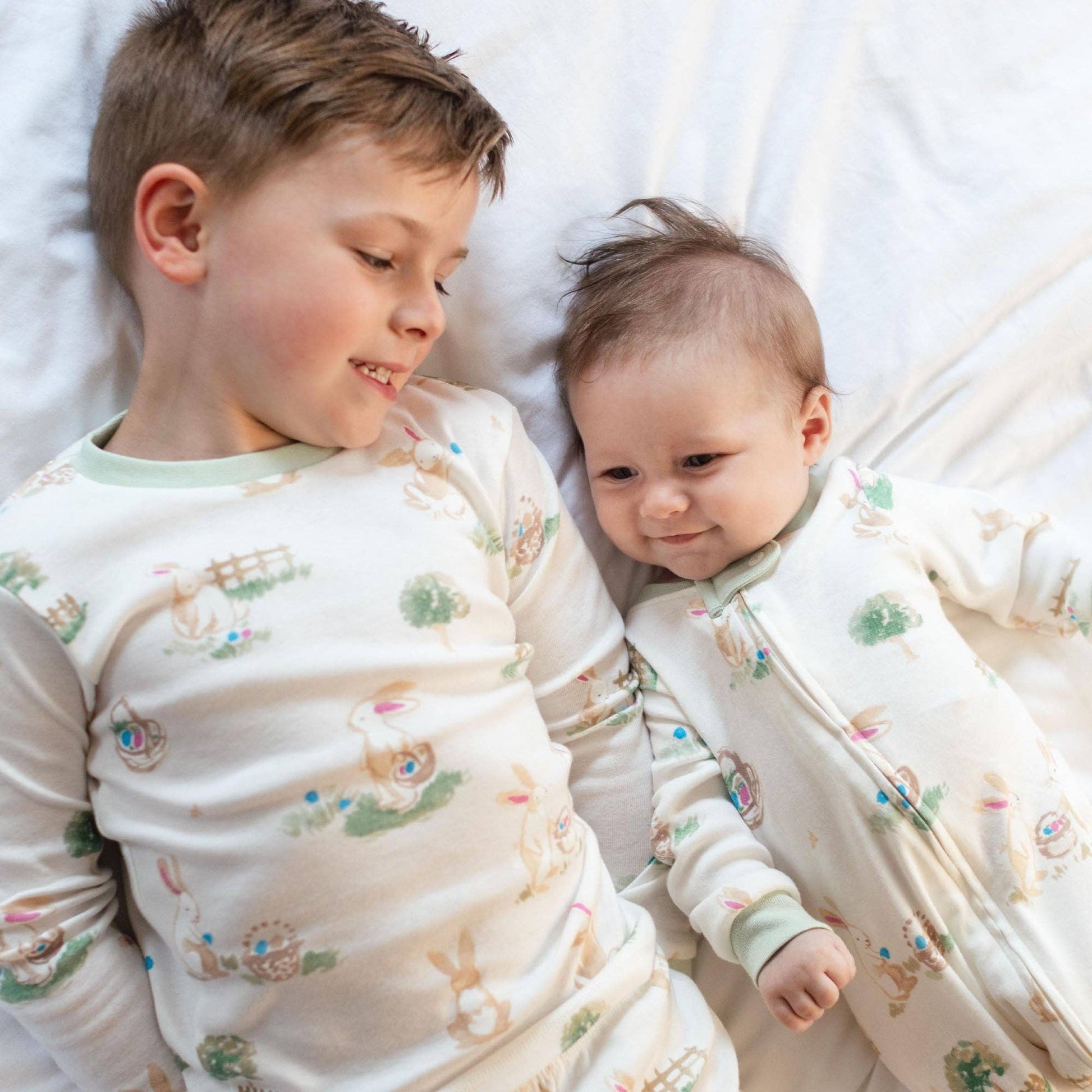 Two children in matching pajamas lying on a white bed.