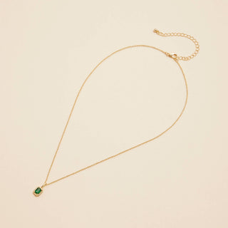 Gold birthstone pendant necklace on a beige background. 