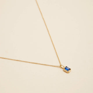 Gold birthstone pendant necklace on a beige background. 