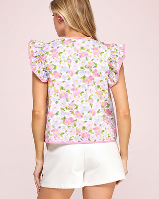 Woman wearing a floral sleeveless top with ruffled sleeves on a pink background