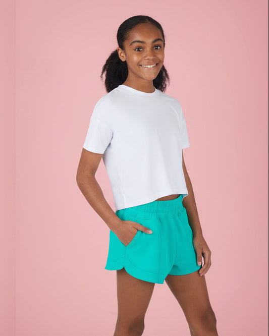 Girl wearing a white t-shirt and teal shorts on a pink background