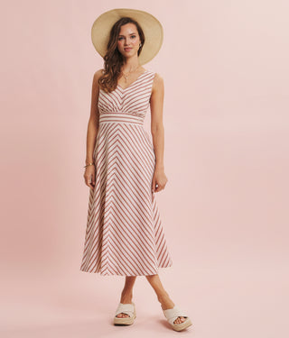 Woman wearing a striped dress and straw hat on a pink background