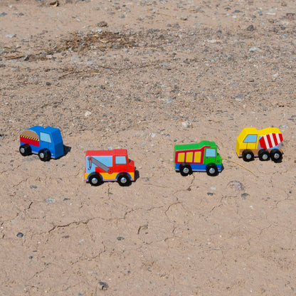 Four colorful toy trucks on a sandy surface